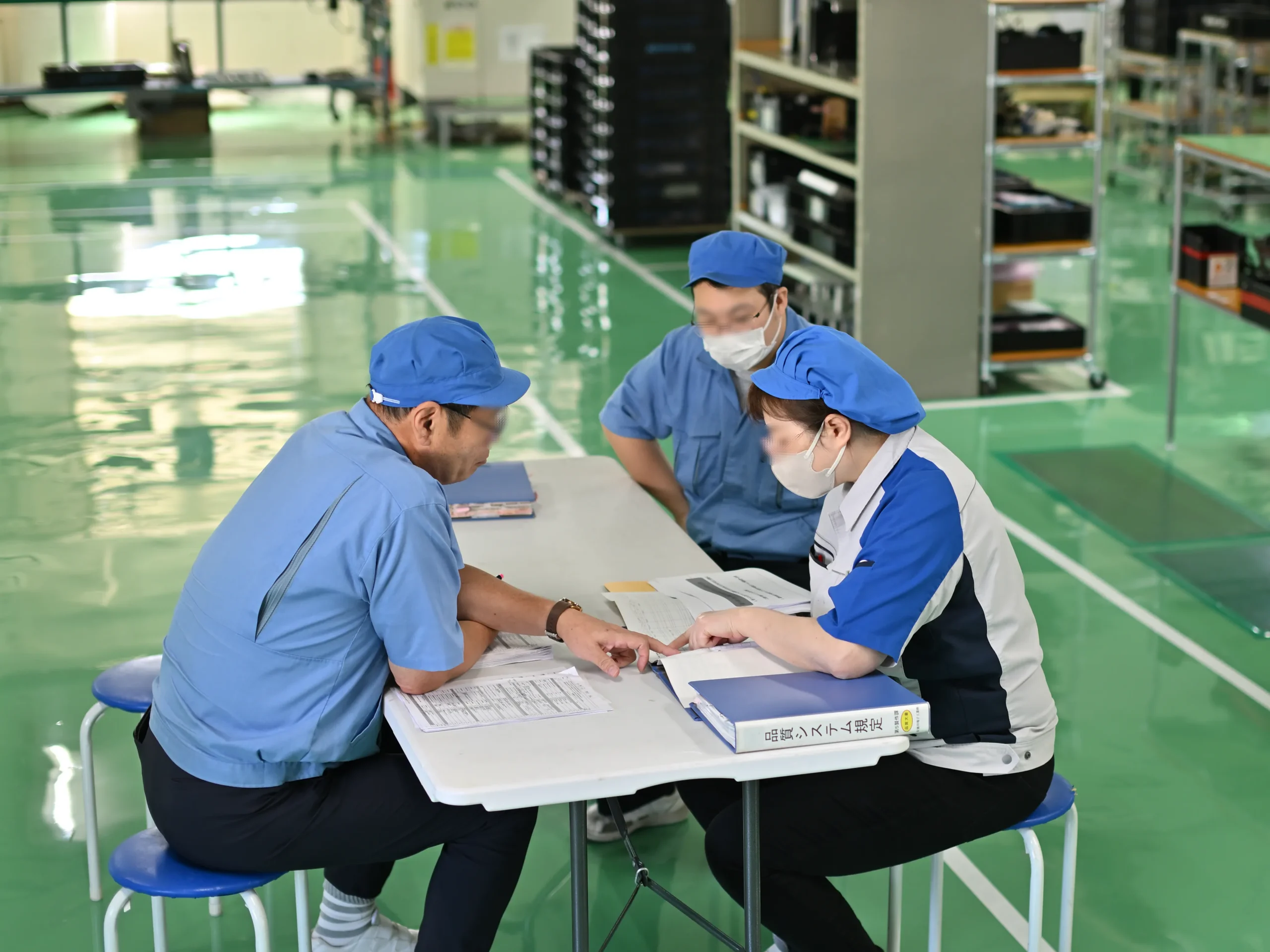 製造現場で品質管理課が現場リーダー、作業者に対して内部監査を行い、品質システム規定の遵守状況を確認している場面