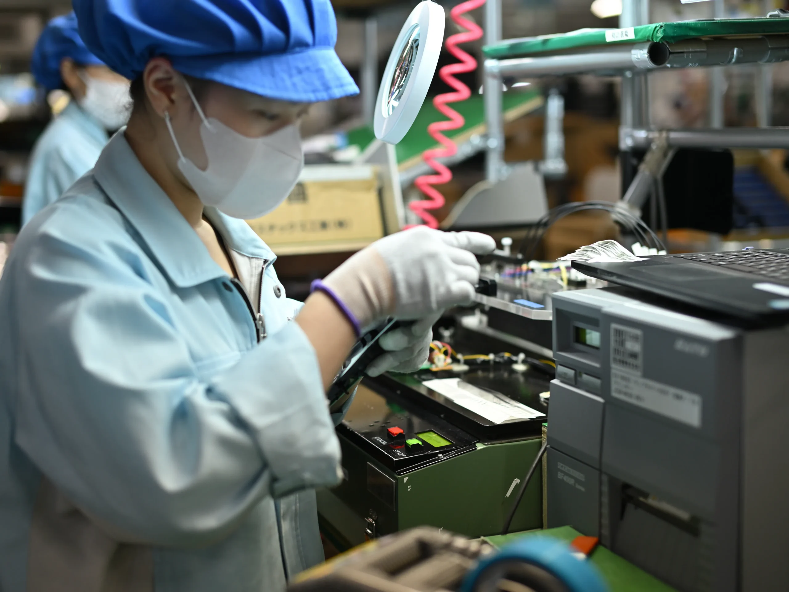 拡大鏡で細部を確認しながら基板の外観検査を行う従業員。監査チェックリストの見直し、監査精度の向上により、これまで見過ごされていた不備や将来のリスクといった改善の機会を積極的に発見しようとする前向きな姿勢が見える