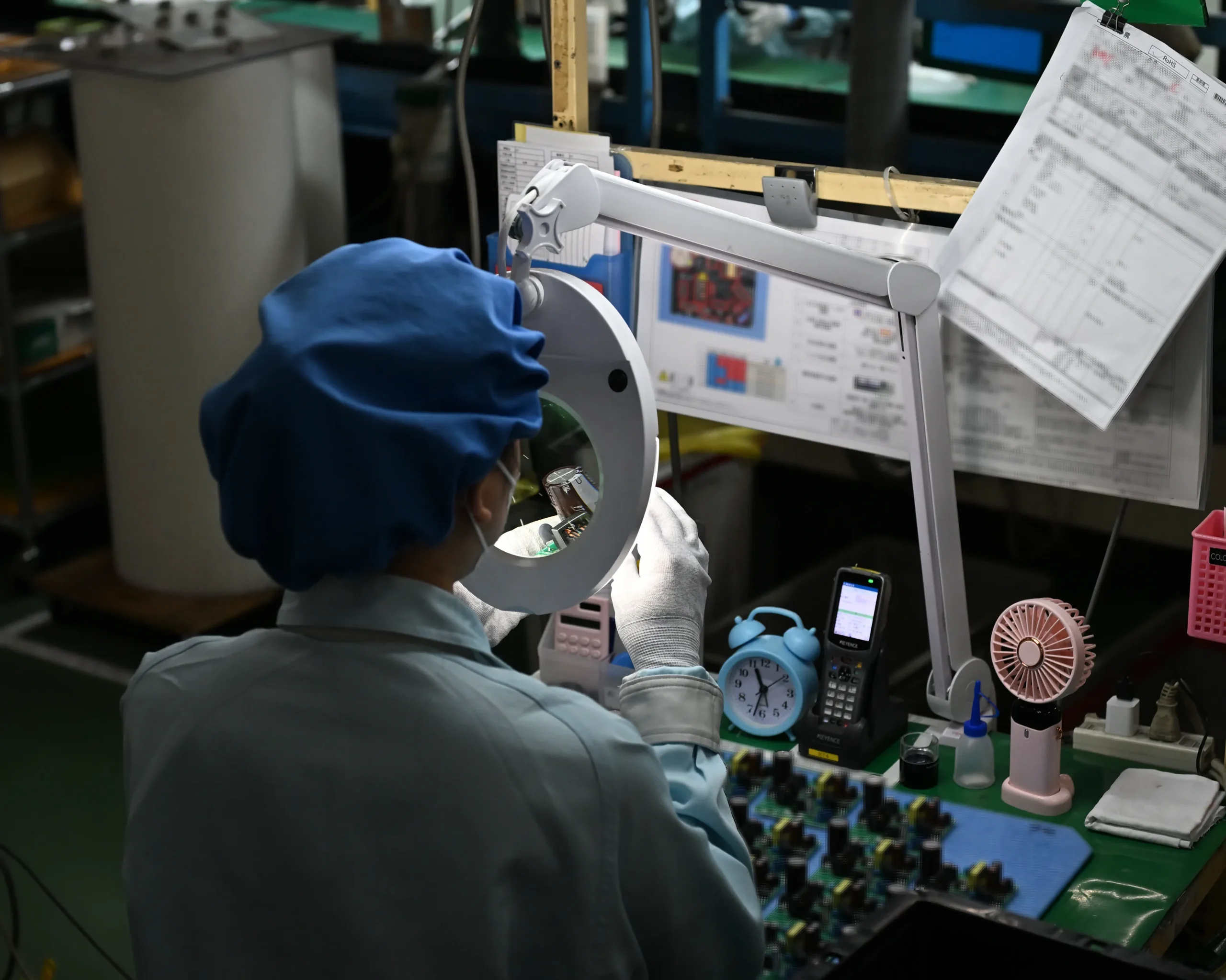 電子部品が実装されたプリント基板を目視検査するアドガワエレクトロニクスの従業員。