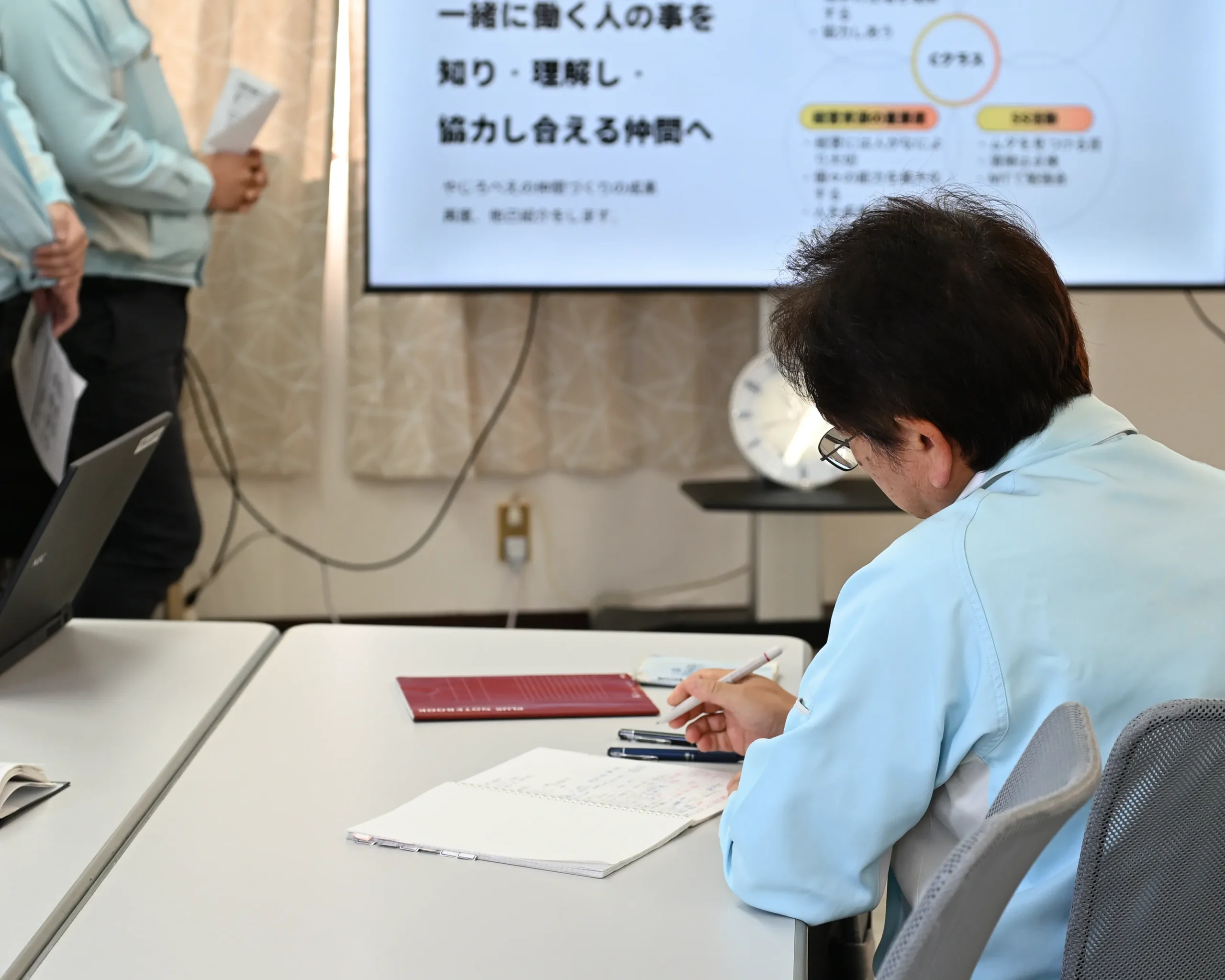 従業員の中間発表を聞いてノートに気づいたことを書き留める社長の様子。