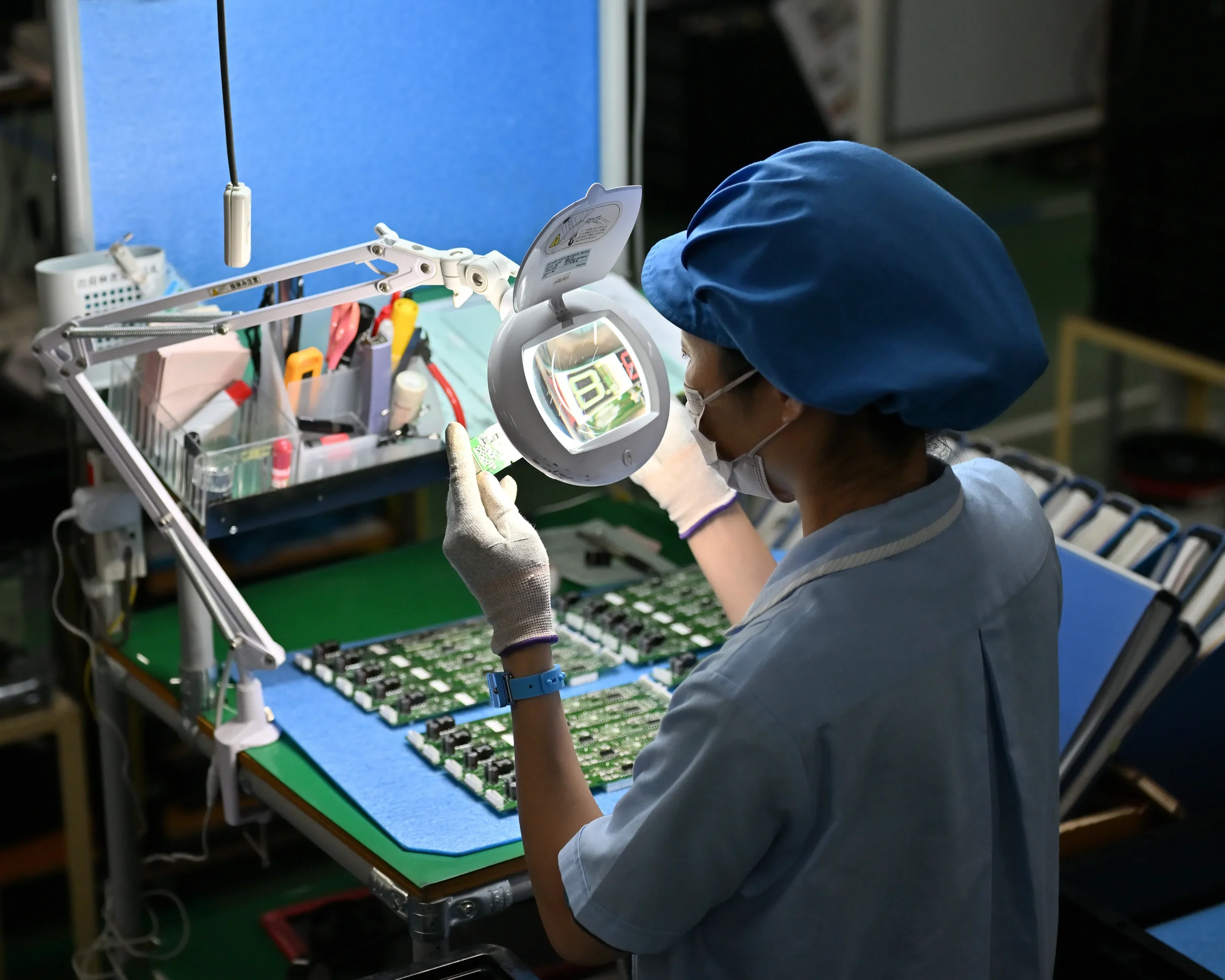 拡大鏡を使って電子部品が実装されたプリント基板一つひとつを目視検査する従業員の様子。